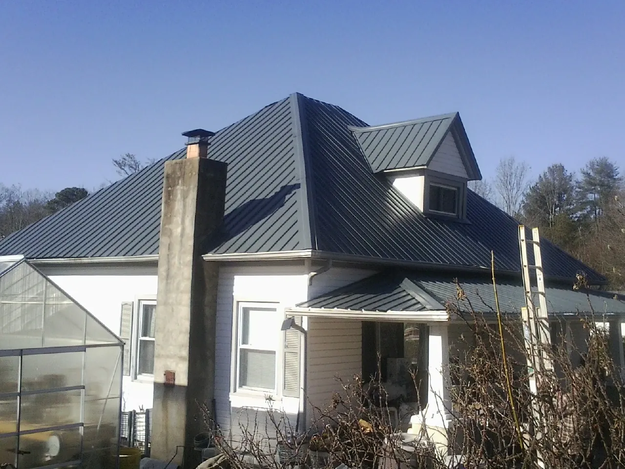 Dark blue standing seam metal roof on a white farmhouse with dormer — Slate & Tile Roof Repair by Roofing Brothers in Goldsmith