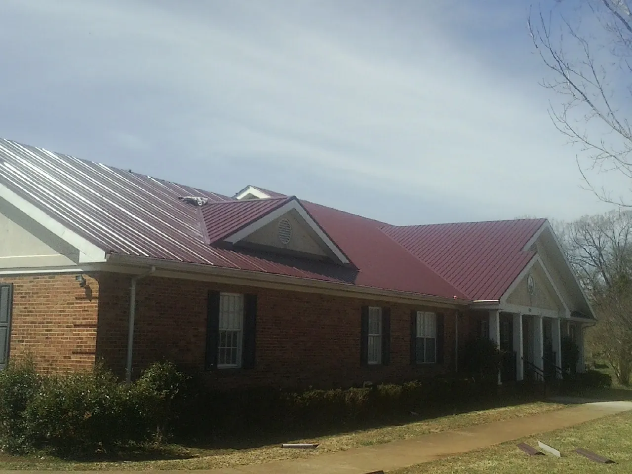 Red metal roof with gabled entries on a long brick building, from a Hail Damage Roof Repair job in Goldsmith