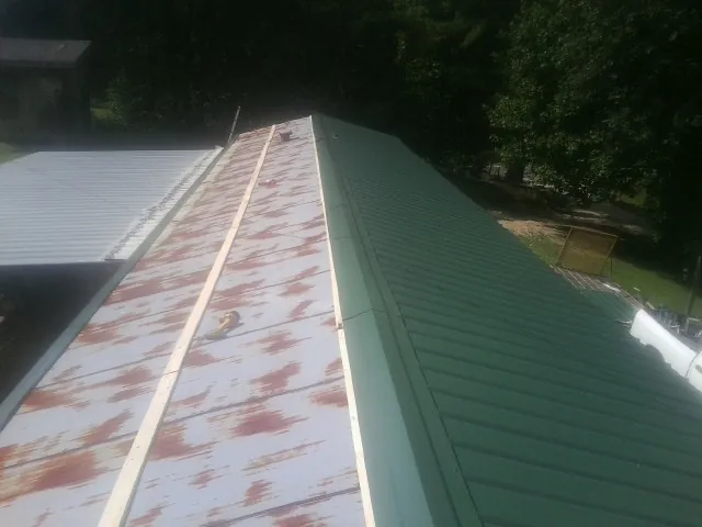 Old rusted panels beside newly installed green metal roofing — Wind Damage Roof Repair by Roofing Brothers in Goldsmith