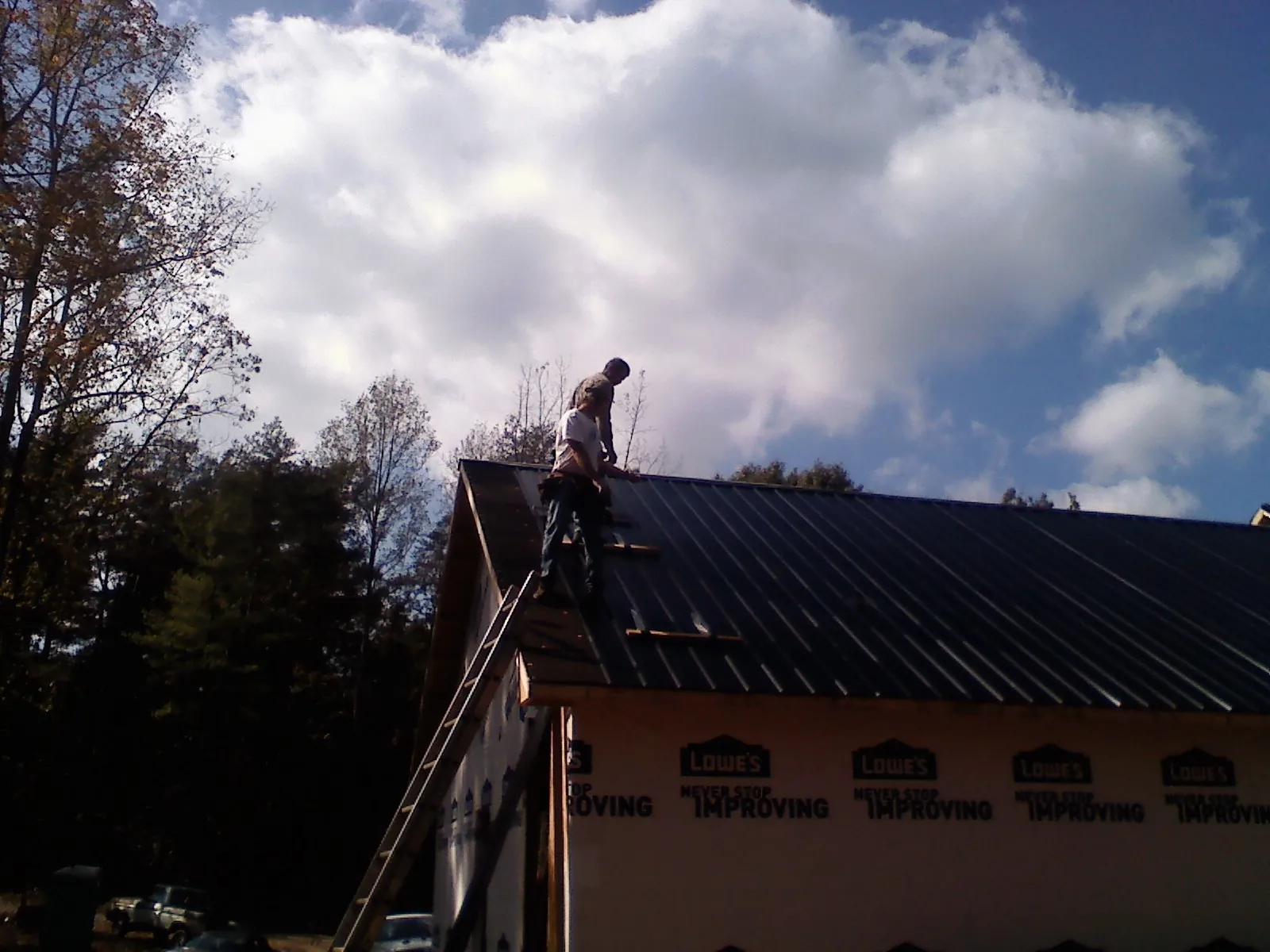 Roofer fastening dark metal panels high against a cloudy sky, from a Roof Inspection job in Goldsmith