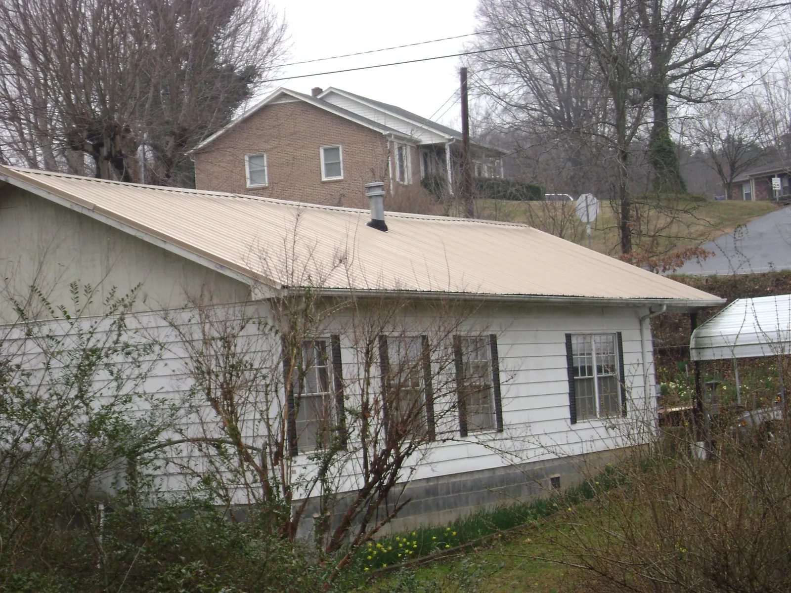 Tan metal roof on a white sided house set into a hillside — Commercial Roofing by Roofing Brothers in Goldsmith