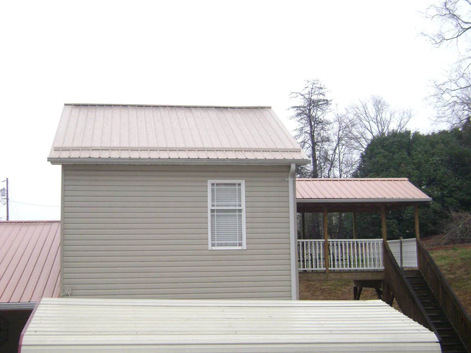 Tan metal roofs on a two story addition and attached porch, from a Roof Replacement job in Goldsmith